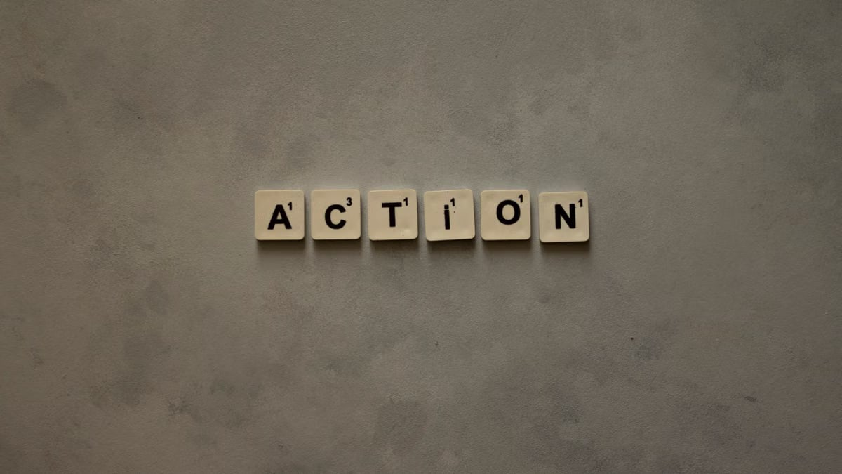 Scrabble tiles forming the word 'Action' on a textured gray surface, conveying motivation.